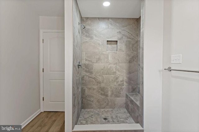 full bathroom with a tile shower, baseboards, and wood finished floors