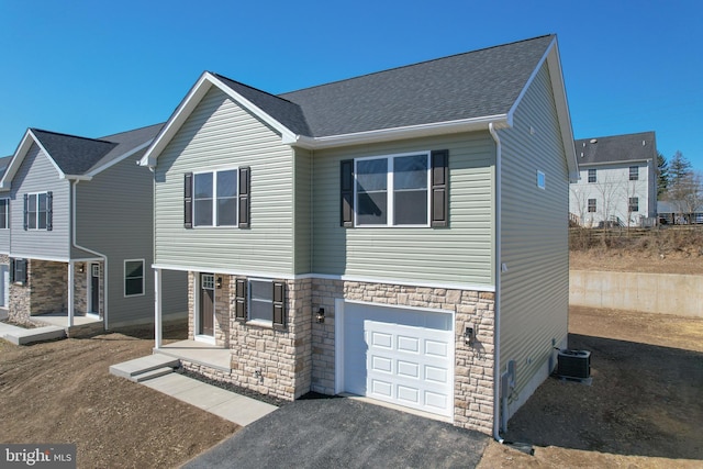 view of front of home with an attached garage, central AC unit, stone siding, and roof with shingles