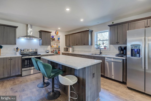 kitchen featuring sink, a kitchen island, light hardwood / wood-style flooring, stainless steel appliances, and wall chimney exhaust hood