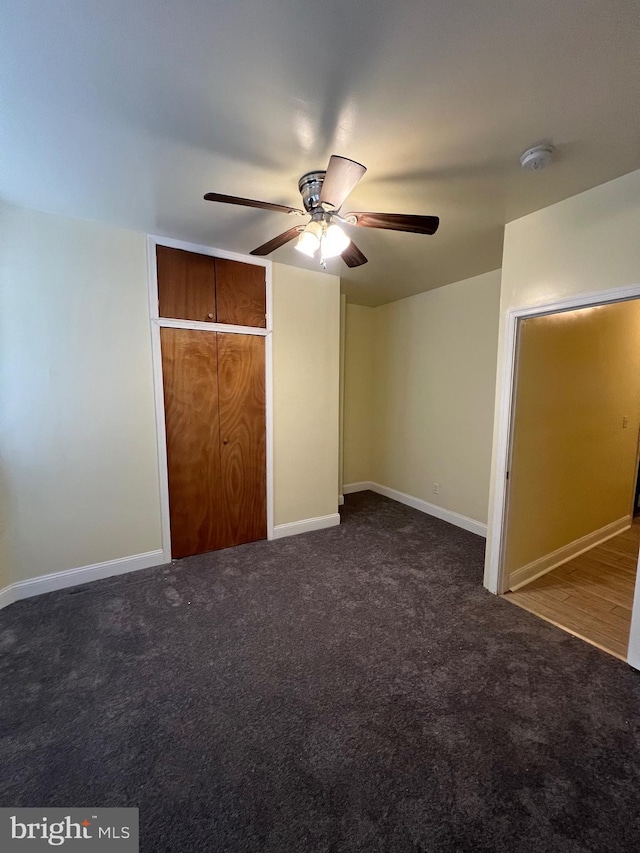 unfurnished bedroom featuring a closet, dark carpet, and ceiling fan