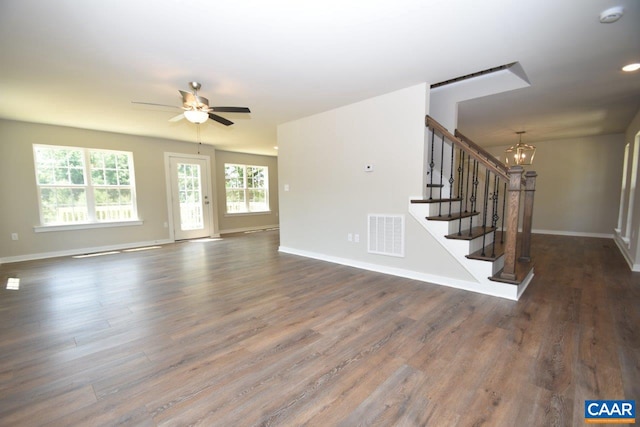 unfurnished living room with ceiling fan with notable chandelier and dark wood-type flooring