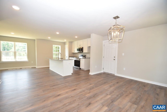 kitchen with dark wood-type flooring, hanging light fixtures, stainless steel appliances, a kitchen island with sink, and white cabinets