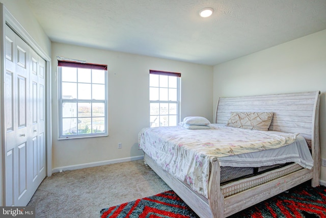 bedroom featuring a textured ceiling, multiple windows, a closet, and light colored carpet