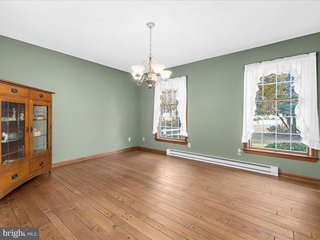 spare room with hardwood / wood-style flooring, a baseboard radiator, and an inviting chandelier