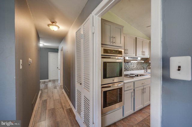 kitchen with light hardwood / wood-style floors, tasteful backsplash, stainless steel double oven, white gas cooktop, and vaulted ceiling