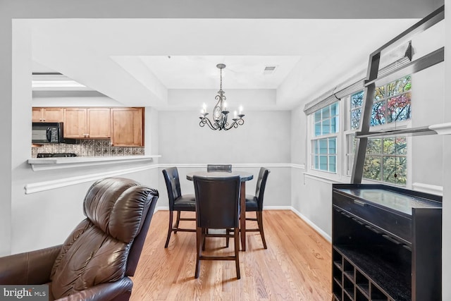 dining space featuring light wood-type flooring, a chandelier, and a raised ceiling