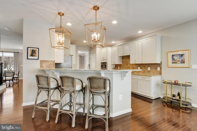 kitchen with kitchen peninsula, hanging light fixtures, light stone counters, white cabinets, and a breakfast bar area