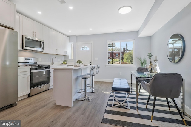 kitchen with a kitchen breakfast bar, stainless steel appliances, a center island, light wood-type flooring, and white cabinets