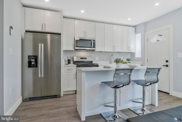 kitchen with a breakfast bar, appliances with stainless steel finishes, white cabinetry, and an island with sink