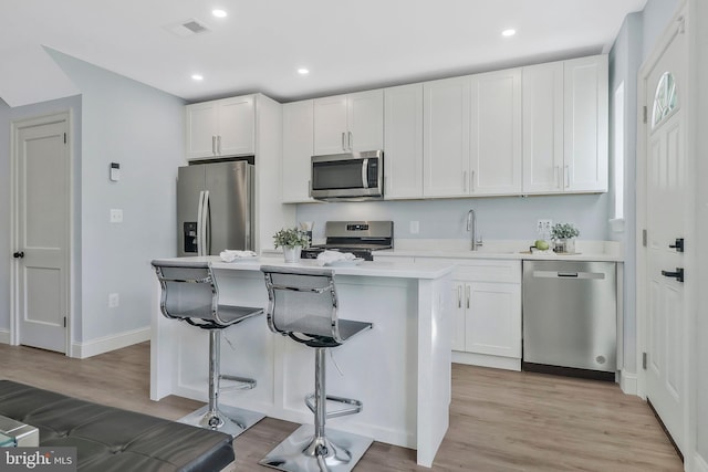 kitchen with a kitchen bar, light wood-type flooring, a center island, stainless steel appliances, and white cabinets