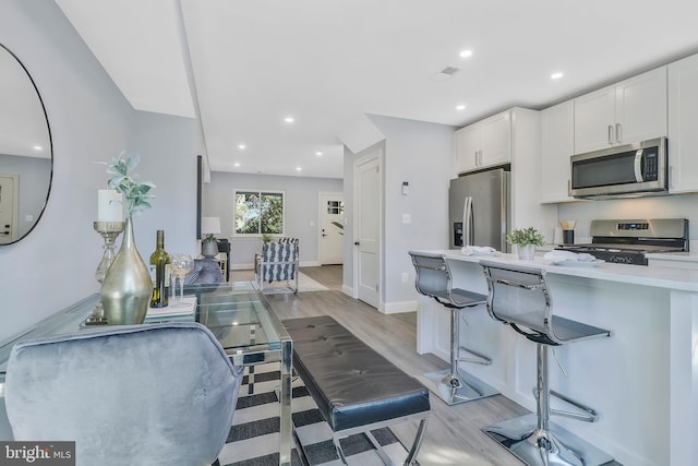 kitchen with a breakfast bar area, appliances with stainless steel finishes, light wood-type flooring, and white cabinets