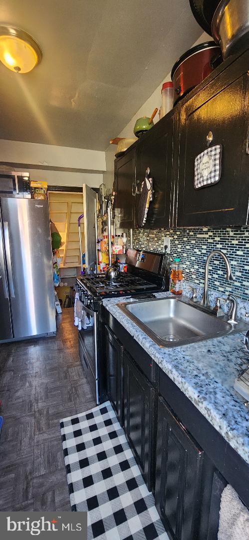 kitchen with sink, appliances with stainless steel finishes, light stone counters, and tasteful backsplash