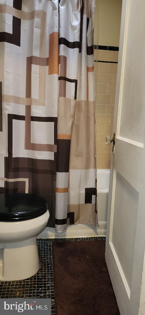 bathroom with shower / tub combo with curtain, tile patterned flooring, and toilet