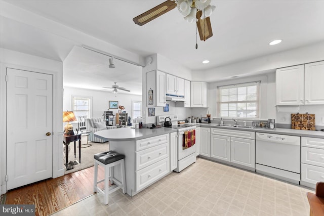 kitchen with white appliances, sink, white cabinets, kitchen peninsula, and light hardwood / wood-style flooring