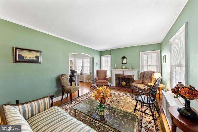 living room with crown molding, hardwood / wood-style floors, a brick fireplace, and plenty of natural light