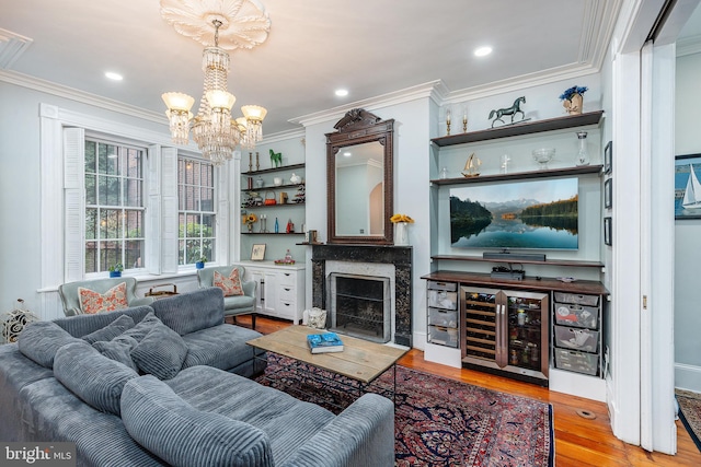 living room with light hardwood / wood-style floors, a premium fireplace, a notable chandelier, ornamental molding, and wine cooler