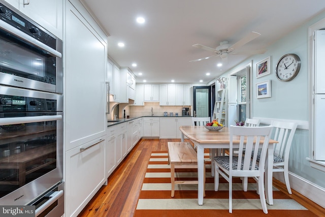 kitchen featuring white cabinets, decorative backsplash, sink, ceiling fan, and light wood-type flooring