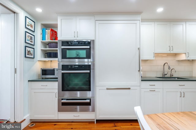 kitchen featuring white cabinetry, stainless steel double oven, tasteful backsplash, and sink