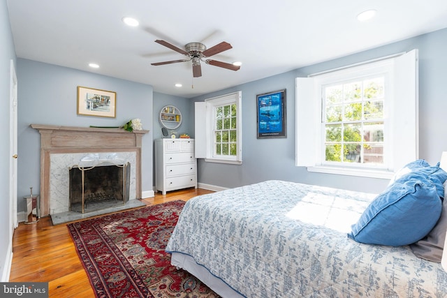 bedroom featuring light hardwood / wood-style floors, ceiling fan, and a premium fireplace