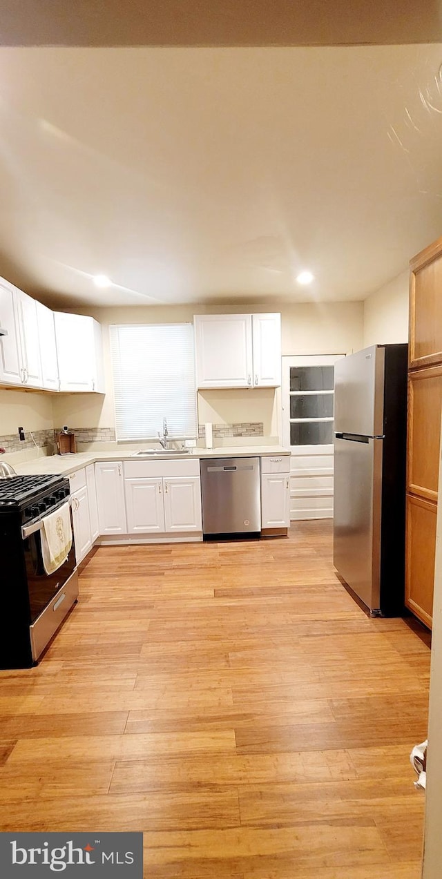 kitchen with light hardwood / wood-style floors, white cabinets, stainless steel appliances, and sink