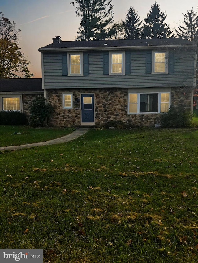 colonial house featuring a yard, stone siding, and a chimney