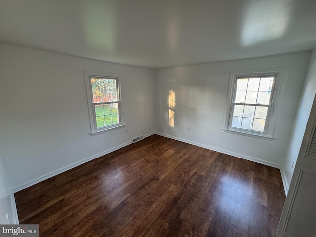empty room with visible vents, baseboards, and dark wood-style floors