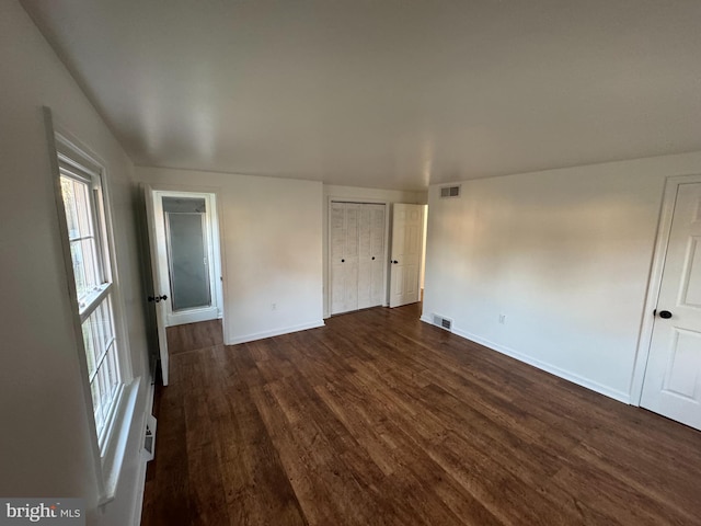 unfurnished bedroom with multiple windows, visible vents, baseboards, and dark wood-type flooring