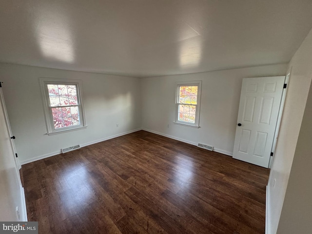 empty room featuring dark wood-type flooring and a healthy amount of sunlight