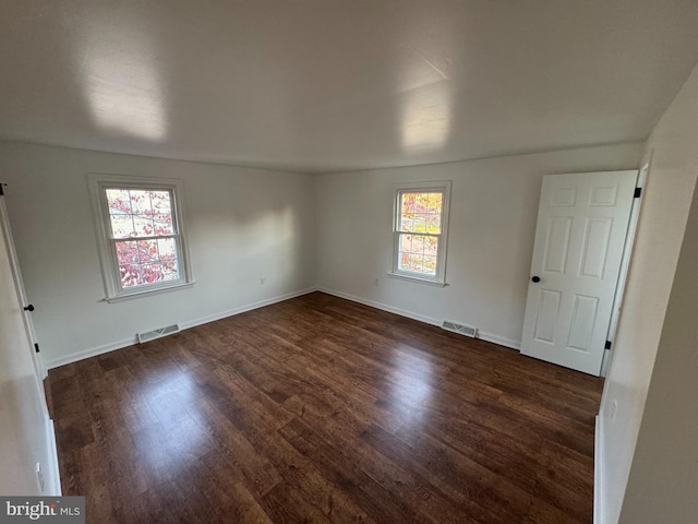 unfurnished room with baseboards, visible vents, and dark wood finished floors