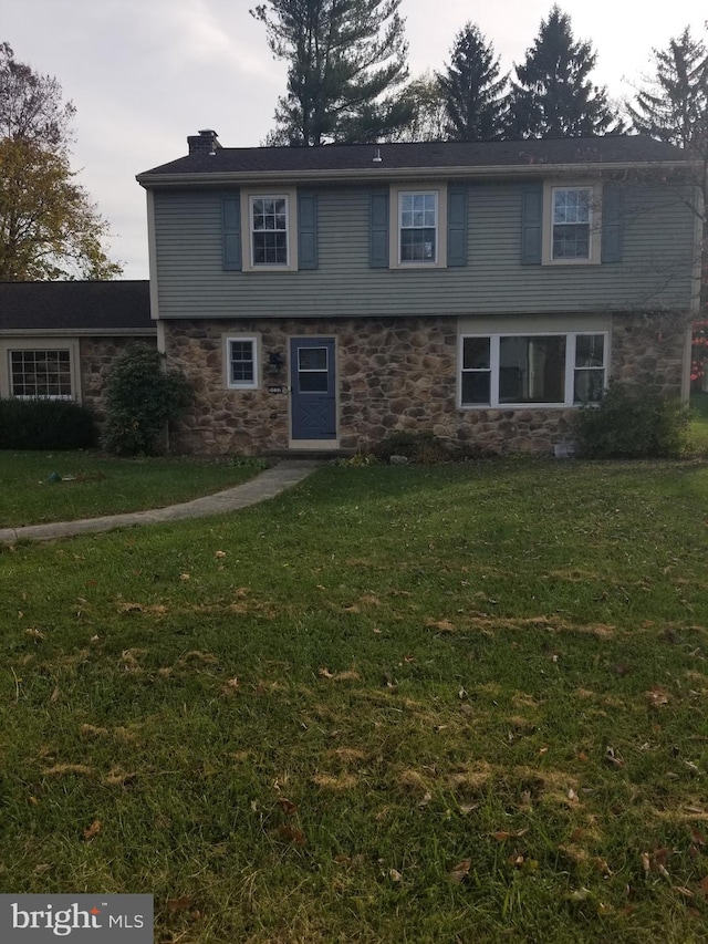 colonial house featuring stone siding, a chimney, and a front yard