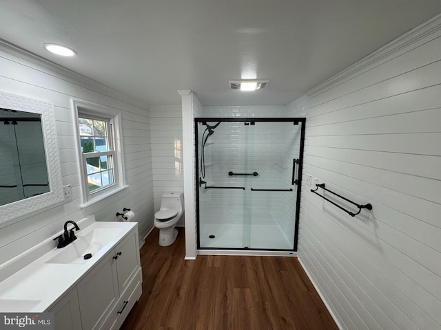 bathroom with a stall shower, toilet, ornamental molding, vanity, and wood finished floors