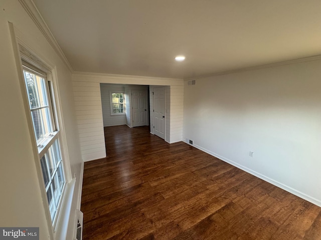 spare room with crown molding, visible vents, baseboards, and dark wood-style floors