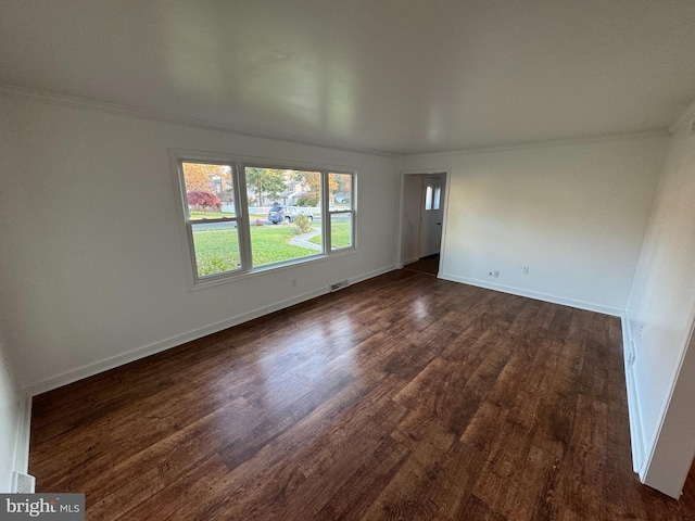 empty room with crown molding, baseboards, dark wood-type flooring, and visible vents