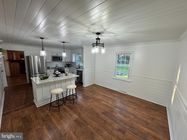 kitchen featuring dark wood-type flooring, hanging light fixtures, a breakfast bar, and stainless steel appliances