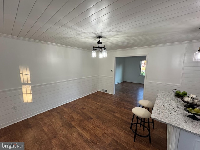 unfurnished dining area with dark wood-type flooring, wooden walls, a chandelier, and ornamental molding