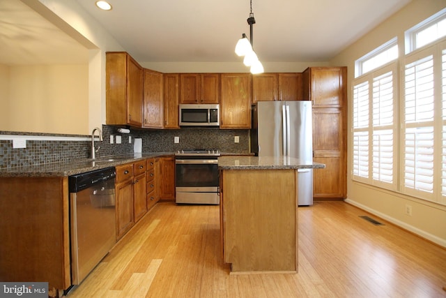 kitchen with appliances with stainless steel finishes, dark stone counters, sink, pendant lighting, and a center island