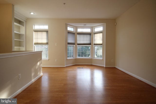 spare room featuring built in features and light hardwood / wood-style flooring