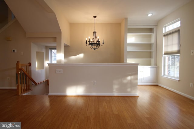 spare room with a notable chandelier, built in shelves, and light hardwood / wood-style flooring