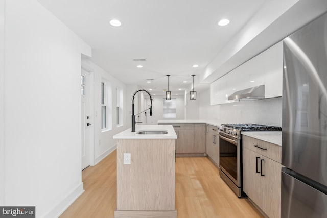 kitchen featuring hanging light fixtures, a kitchen island with sink, light brown cabinetry, light hardwood / wood-style flooring, and stainless steel appliances