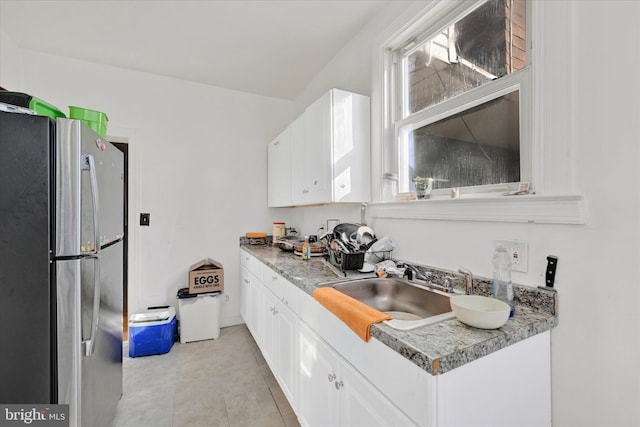 kitchen with white cabinets, sink, light tile patterned floors, and stainless steel refrigerator