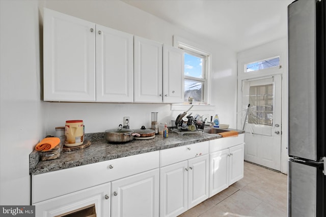 kitchen featuring stainless steel fridge, white cabinets, sink, and light tile patterned floors