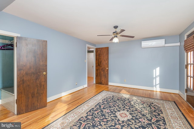 unfurnished room with ceiling fan, wood-type flooring, and a wall mounted air conditioner