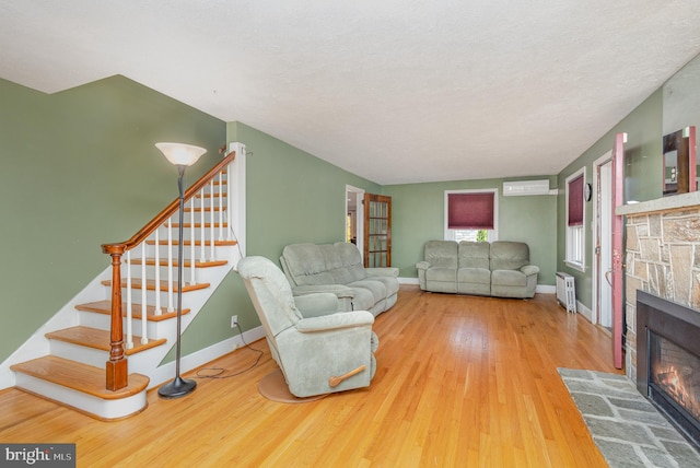 living room featuring a wall mounted AC, a textured ceiling, hardwood / wood-style floors, a stone fireplace, and radiator heating unit