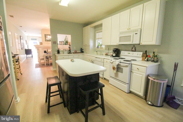 kitchen featuring a kitchen island, white appliances, a breakfast bar, white cabinets, and light hardwood / wood-style floors