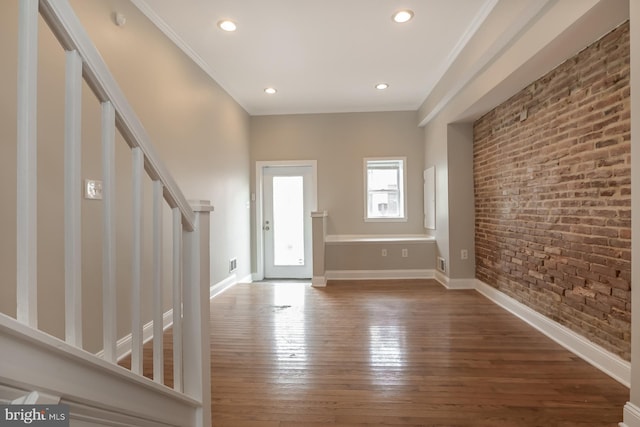 entrance foyer with hardwood / wood-style flooring, baseboards, brick wall, ornamental molding, and stairs