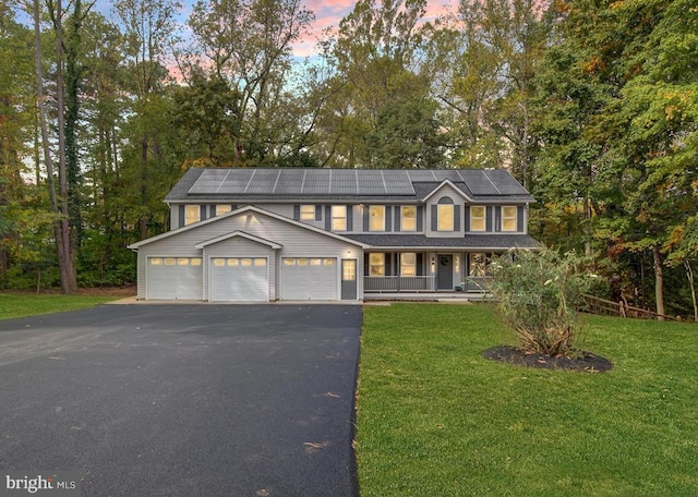 view of front of property with a yard, covered porch, a garage, and solar panels