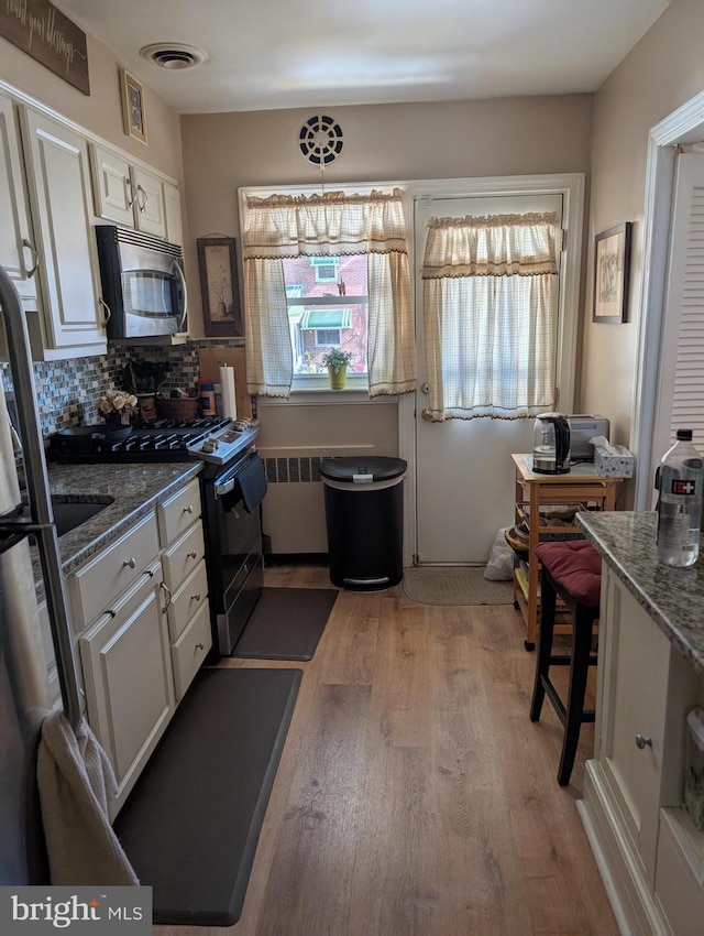 kitchen featuring tasteful backsplash, stainless steel appliances, decorative light fixtures, white cabinets, and hardwood / wood-style flooring