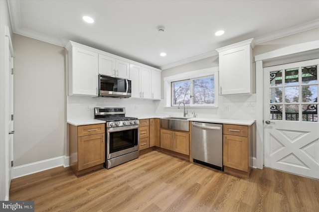 kitchen with sink, light hardwood / wood-style flooring, ornamental molding, appliances with stainless steel finishes, and white cabinetry