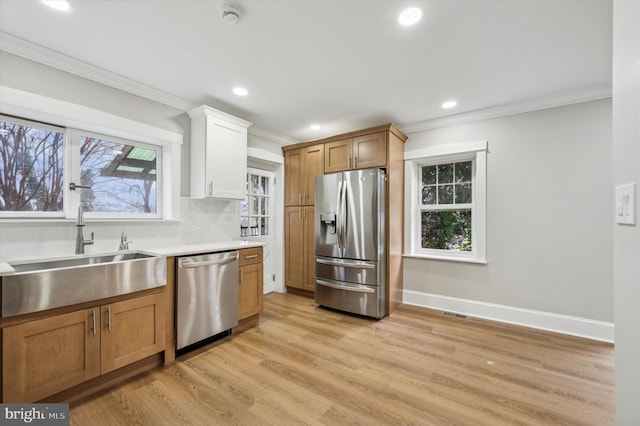 kitchen featuring stainless steel appliances, crown molding, sink, light hardwood / wood-style floors, and white cabinetry