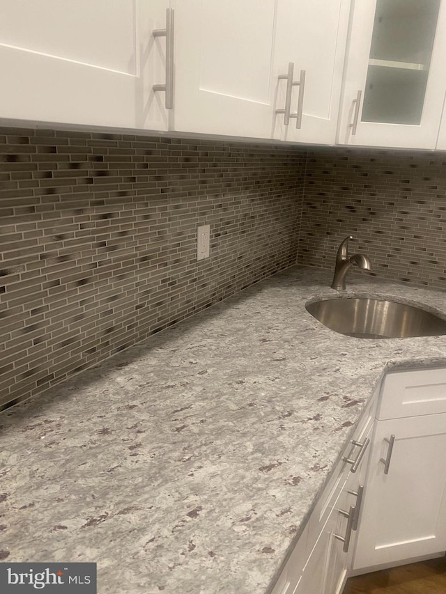 kitchen with decorative backsplash, white cabinets, sink, and light stone counters